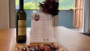 A bottle of wine, a menu, and a plate of chocolates on a table with a view of mountains through a window. - Apartment in Saalfelden Near Ski Slopes (Saalfelden am Steinernen Meer)