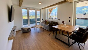 A modern living room with a wooden ceiling, a sofa, a dining table, and a TV mounted on the wall. - Apartment in Saalfelden Near Ski Slopes (Saalfelden am Steinernen Meer)
