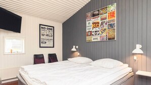 Una cama bien hecha en una habitación con pared gris, un collage de carteles y una ventana con persianas.