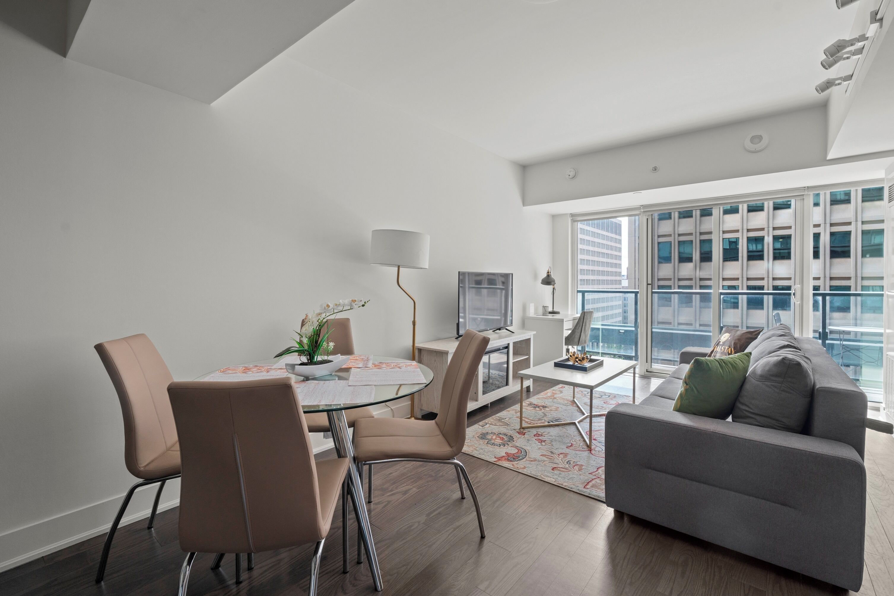 A modern living room with a dining table, chairs, a sofa, and a large window with a city view.