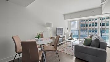 A modern living room with a dining table, chairs, a sofa, and a large window with a city view.