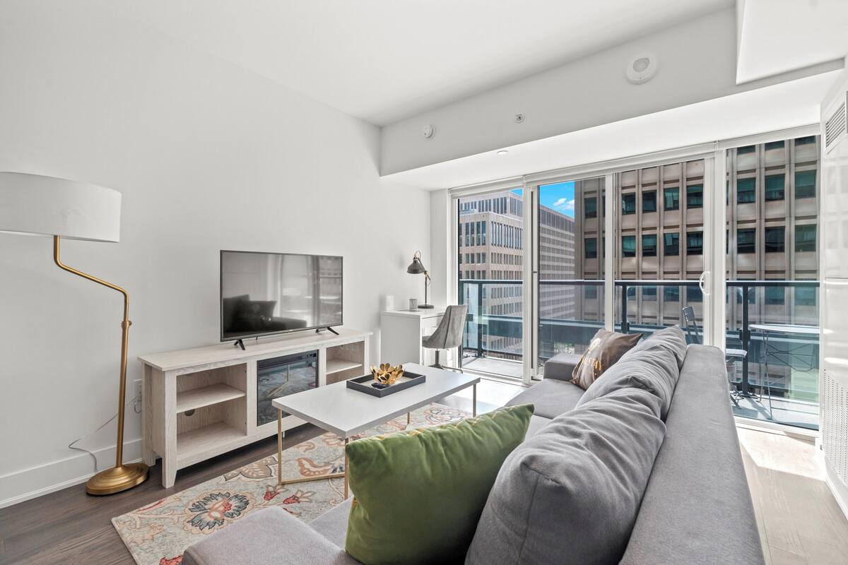 A modern living room with a large window, a flat-screen TV, a white console table, and a grey sofa.