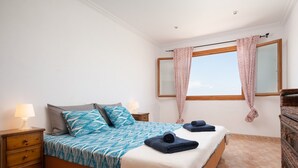 Un dormitorio con una cama, dos mesitas de noche, una ventana con cortinas y un aparador de madera.