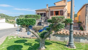 Una villa de estilo mediterráneo con fachada de piedra, tejado de tejas y un pequeño jardín con un árbol.
