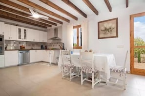 A kitchen with white cabinets, a dining table with chairs, a ceiling fan, and a window with curtains. - Gina - Villa With Private Pool In Algaida (Algaida, Illes Balears)