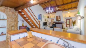 A rustic kitchen with a stone wall, wooden counter, and tiled floor.