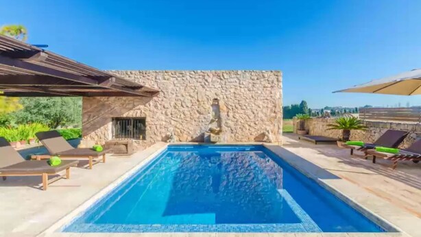 A swimming pool with lounge chairs and a stone wall.