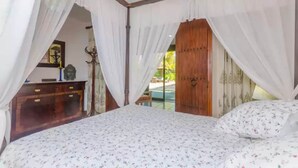A bedroom with a canopy bed, wooden wardrobe, and a view of the outdoors.