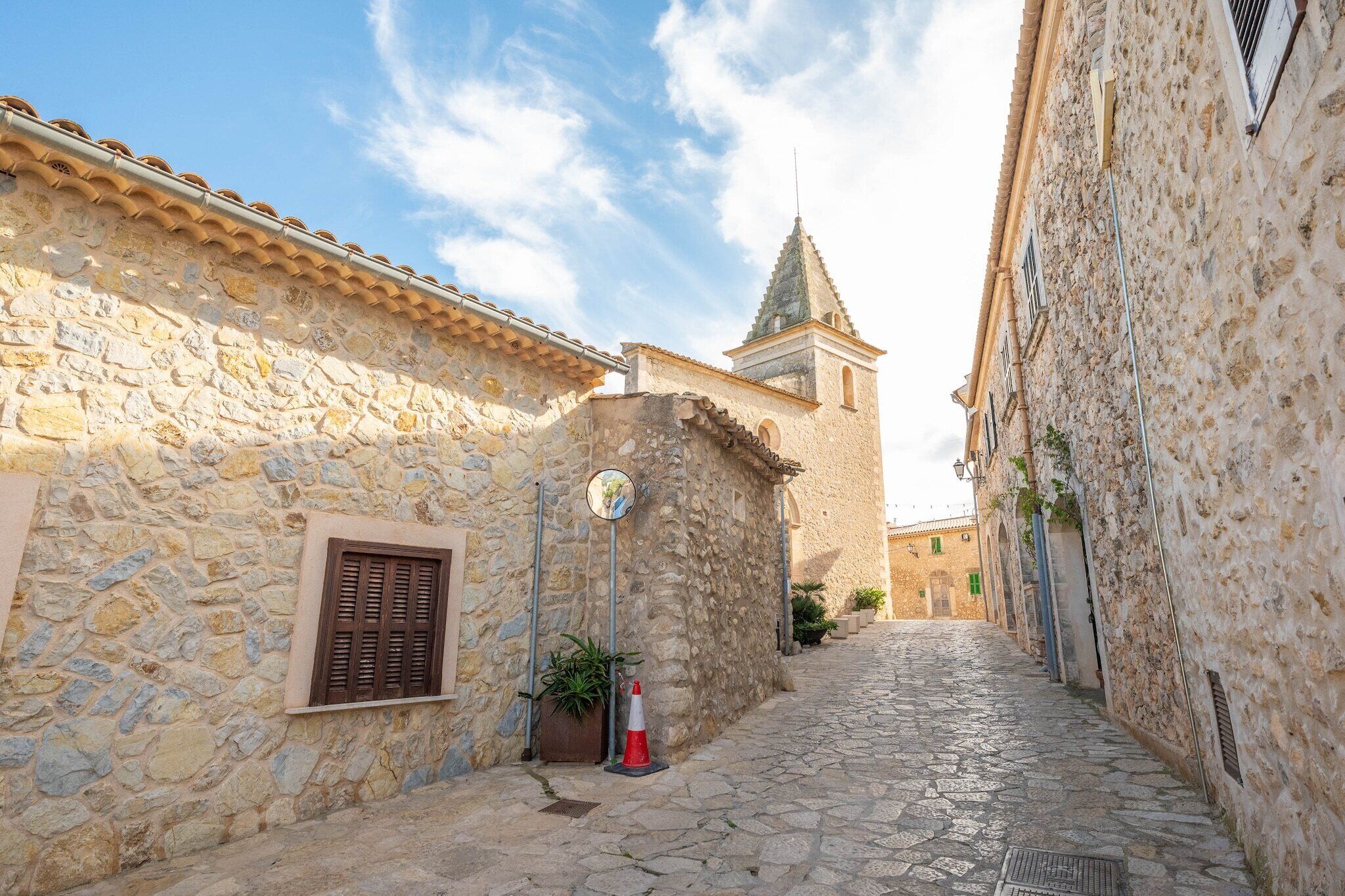 A narrow cobblestone street flanked by stone buildings with a church tower in the background.