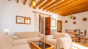 A living room with a wooden ceiling, beige sofas, a glass coffee table, and a dining area with wooden chairs and a table. - Can Salvador - Villa With Private Pool In Moscari (Moscari (selva), Illes Balears)