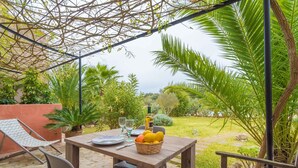 An outdoor patio with a wooden table, chairs, and a basket of fruit.