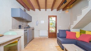 A compact living space with a kitchenette, a sofa with colorful cushions, a wooden table, and a view through a door to an outdoor area.
