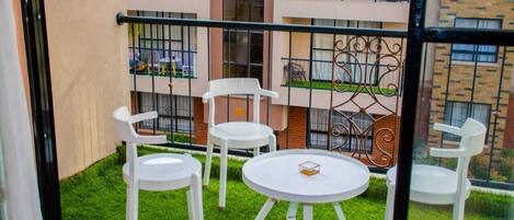 Ein Balkon mit weißen Stühlen und einem kleinen Tisch, umgeben von einem Metallgeländer.
