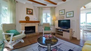 A living room with a fireplace, two armchairs, a television, and a glass coffee table. - Gladiolo - Villa With Private Pool (El Tosalet - Xàbia, Alicante)
