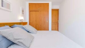 A bedroom with a bed, pillows, a nightstand, and a wooden wardrobe. - Llepol - Apartment In Port D'alcúdia. Free Wifi (Port D'alcÚdia, Illes Balears)