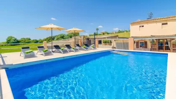 A swimming pool with lounge chairs and umbrellas, surrounded by a building with a flat roof and a fence. - Es Pont Den Teulari Nou - Villa With Private Pool (Manacor, Illes Balears)