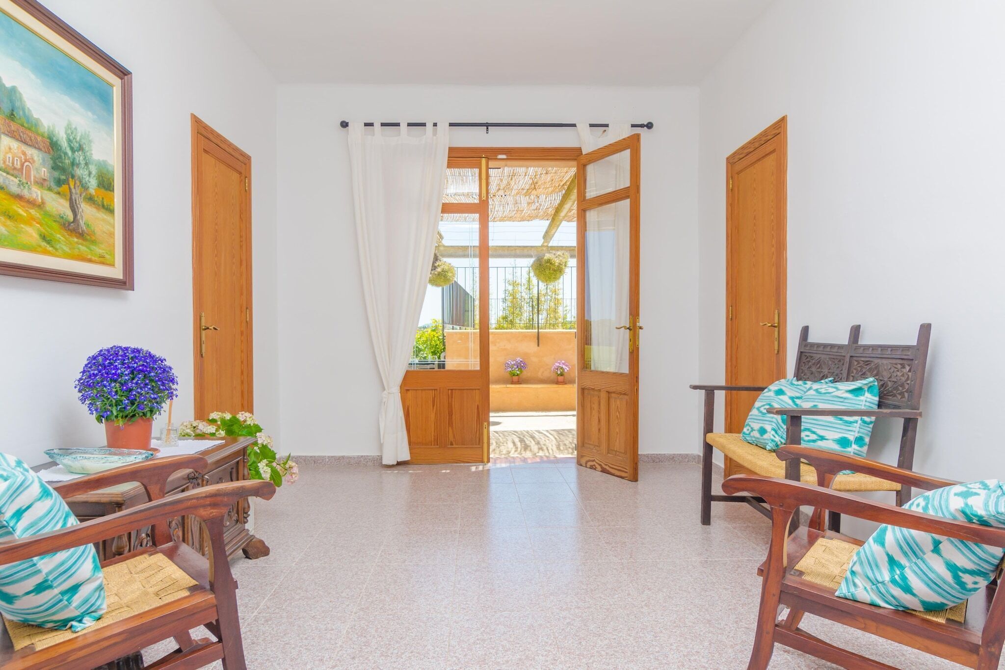 A room with wooden doors, a table with chairs, and a view to an outdoor area with plants.