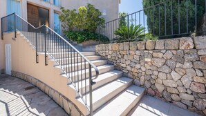 Un escalier en pierre menant à l’entrée d’un bâtiment, avec une rambarde en métal et un mur en pierre d’un côté.