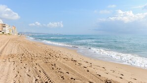 A sandy beach with footprints, a clear sky, and distant buildings.