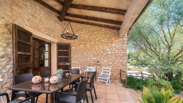 Une terrasse extérieure avec des murs en pierre, une table en bois avec des chaises et un luminaire suspendu.