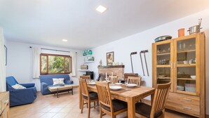 Un coin repas avec une table en bois dressée pour quatre personnes, entourée de chaises. À droite, on aperçoit un canapé bleu et un meuble en bois doté de portes en verre.