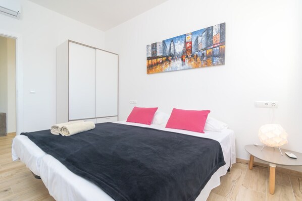 A modern hotel room with a large bed, a painting on the wall, and a bedside table with a lamp.