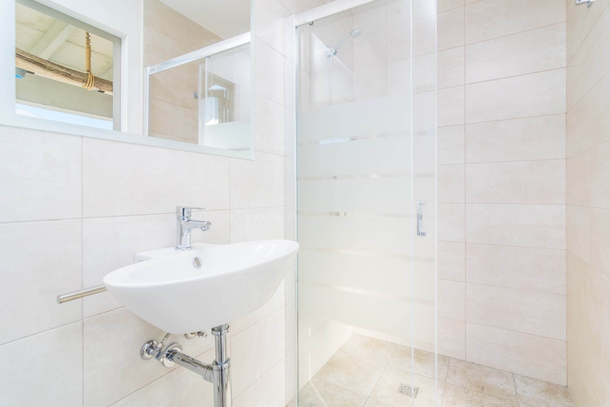 A modern bathroom with a white sink, a glass shower enclosure, and a large mirror.