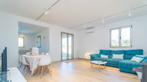 A modern living room with a teal sofa, a dining area with a white table and chairs, and a kitchen visible in the background. - Can Colomer Ferragut  - Villa With Private Pool (Artà, Illes Balears)
