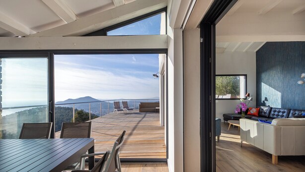 A modern living space with a wooden deck, a dining area, and a sofa set. - Villa Vue Mer 180 - Face aux îles d’Or (Carqueiranne)