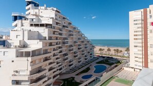 A multi-story hotel with balconies, a swimming pool, and a view of the beach. - Torres Del Mar - Apartment In Grau I Platja (Playa De Gandia, Valencia)