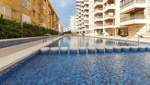 A swimming pool with a tiled floor, surrounded by multi-story buildings with balconies. - Torres Del Mar - Apartment In Grau I Platja (Playa De Gandia, Valencia)