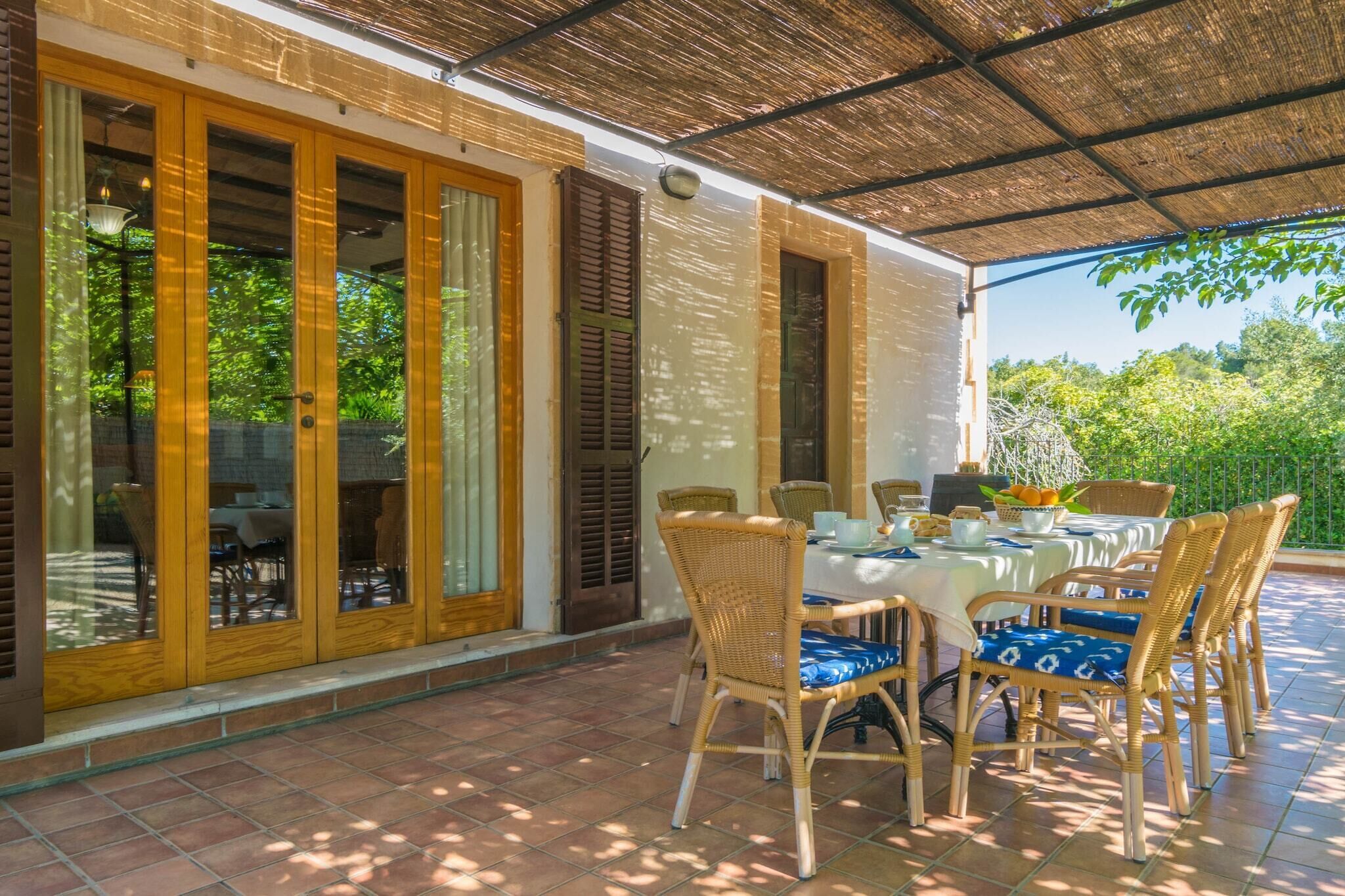 A covered patio with a table set for dining, surrounded by wicker chairs with blue cushions.