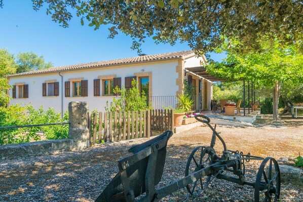 A white building with brown shutters, a wooden fence, and a garden area with a bench and potted plants. - Can Mostatxet - Villa With Private Pool. Free Wifi (Can Picafort, Illes Balears)
