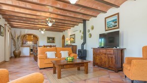 A cozy living room with a sofa, coffee table, and TV. There is a fireplace, wooden cabinets, and a tiled floor. - Can Mostatxet - Villa With Private Pool. Free Wifi (Can Picafort, Illes Balears)