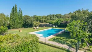 A rectangular swimming pool surrounded by a well-maintained lawn, with a few trees and a thatched-roof structure in the background. - Can Mostatxet - Villa With Private Pool. Free Wifi (Can Picafort, Illes Balears)