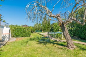 A backyard with a tree, a barbecue grill, and a dining table with chairs. - Can Mostatxet - Villa With Private Pool. Free Wifi (Can Picafort, Illes Balears)