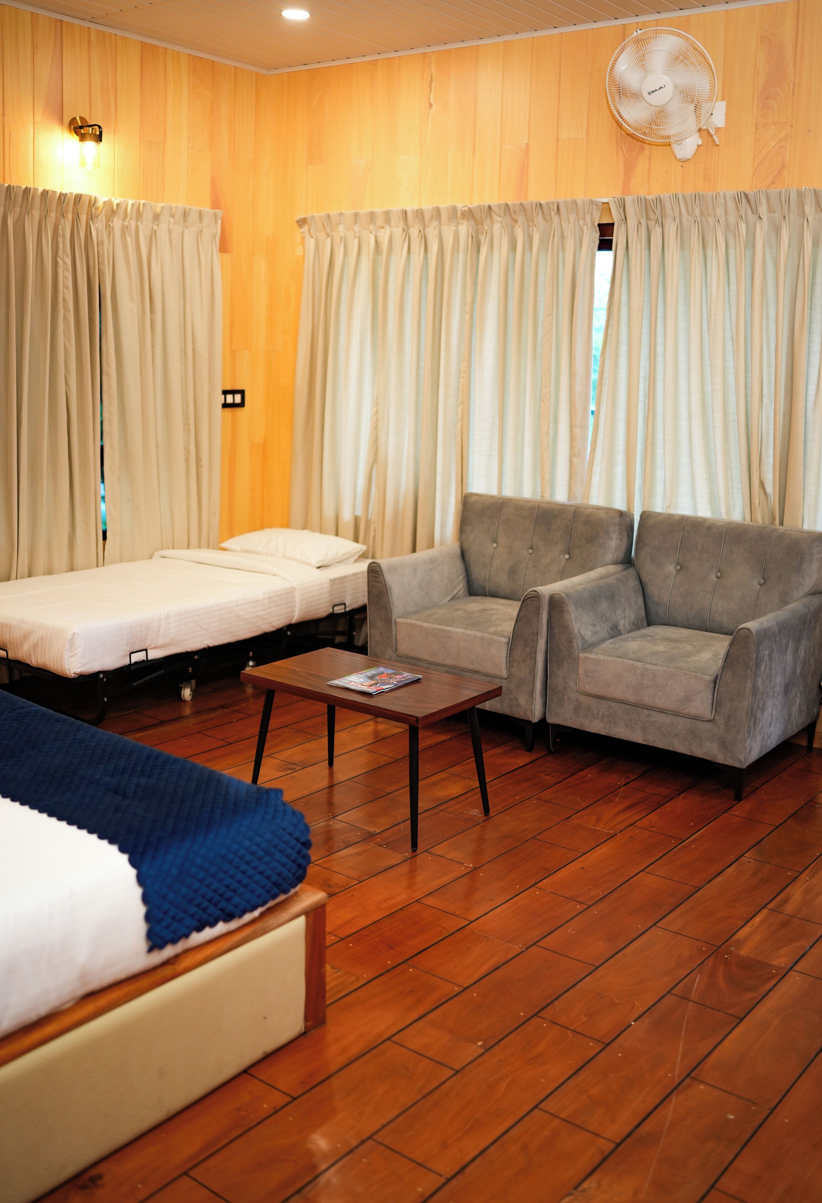 A room with a bed, two sofas, a small table, wooden flooring, and curtains.