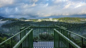 A green metal staircase leading to a platform overlooking a forested valley with mist and clouds above. - Space Rock Resort (Vythiri)