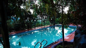 An outdoor swimming pool surrounded by trees and a metal fence. - Space Rock Resort (Vythiri)