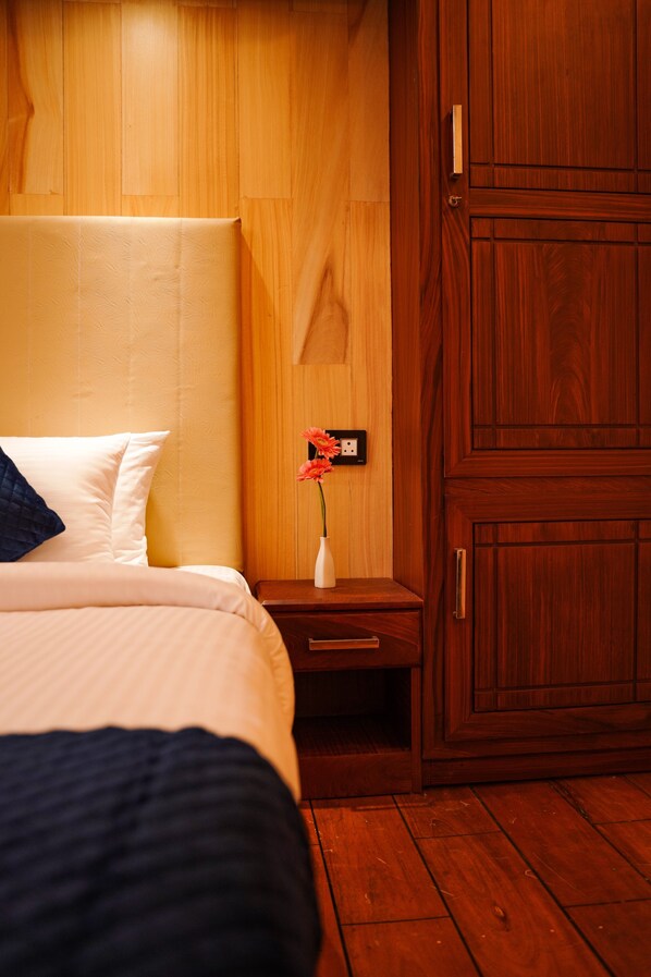 A hotel room with a bed, a nightstand, a vase with flowers, and wooden paneling.