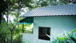 A white wooden cabin with a tiled roof, surrounded by dense forest. - Space Rock Resort (Vythiri)