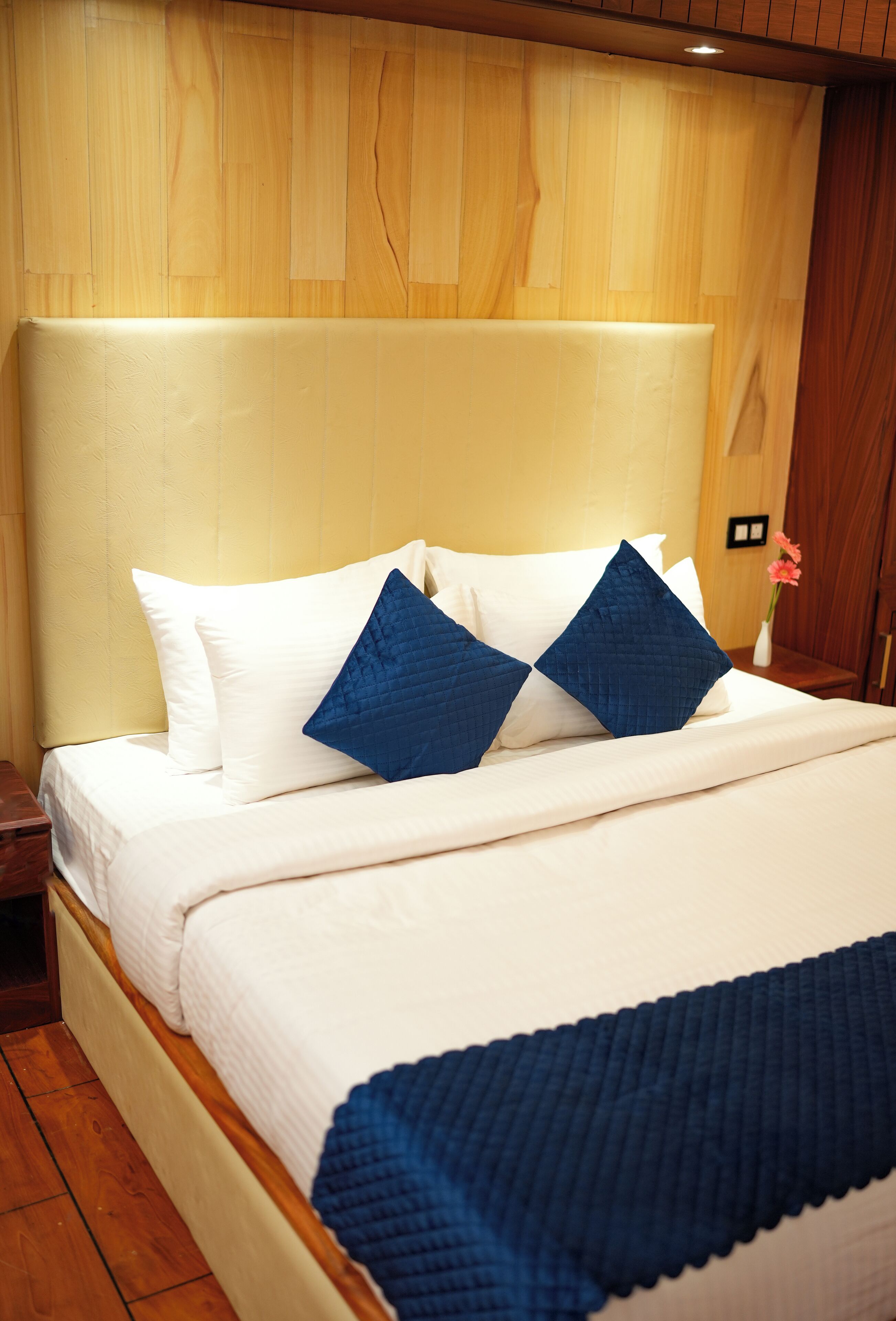 Una cama bien hecha con almohadas blancas y azules, cabecera de madera y suelo de madera.