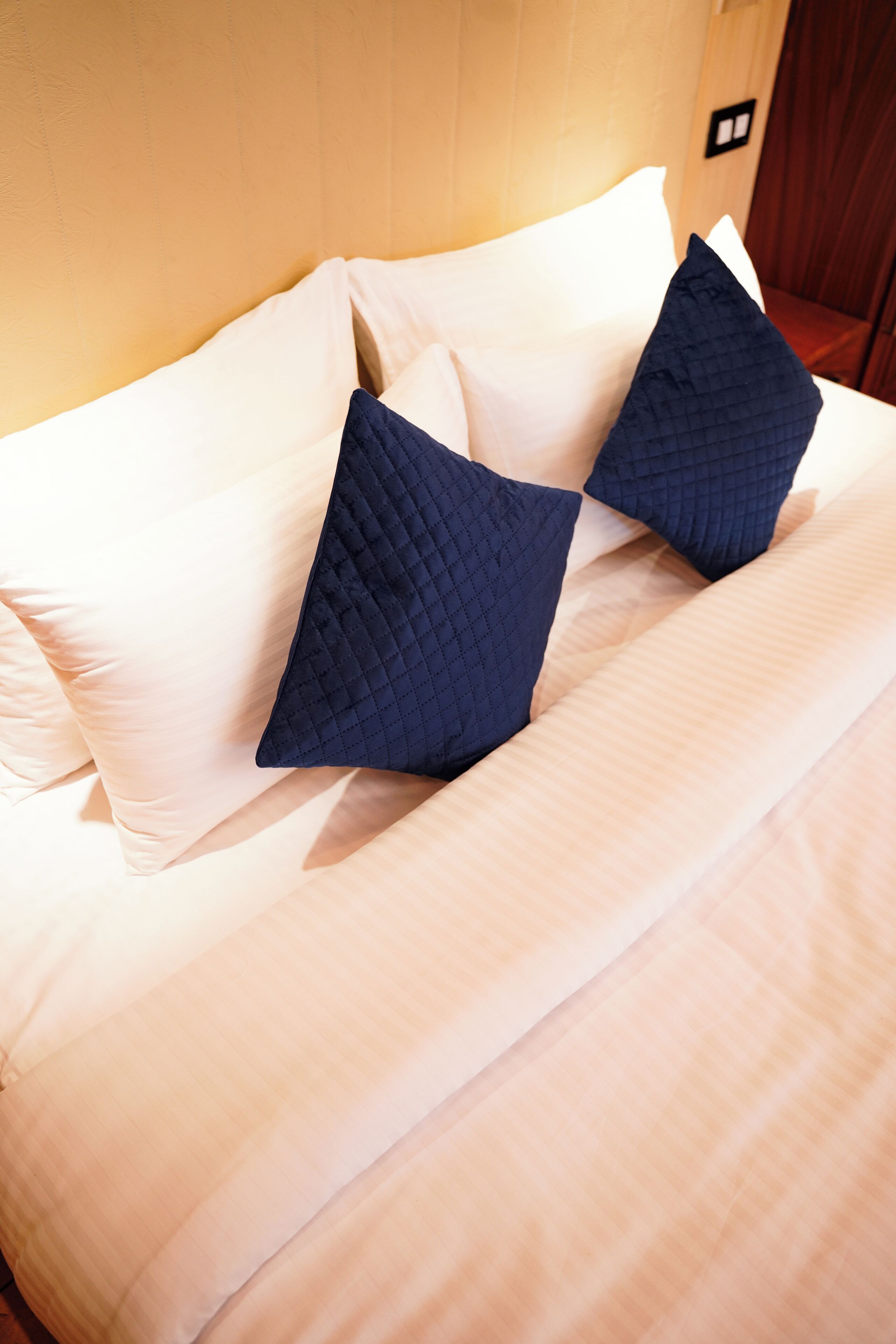 A neatly made bed with two pillows, one dark and one light, in a room with wooden paneling.