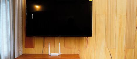 Un mueble de madera para entretenimiento con un televisor de pantalla plana, un pequeño dispositivo blanco en la pared y un banco de madera.
