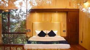 A bedroom with a large bed, wooden walls, and a view of trees through a window. - Space Rock Resort (Vythiri)
