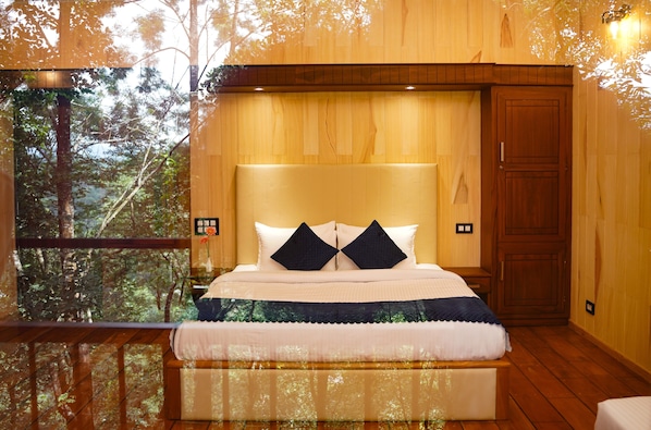 Un dormitorio con una cama grande, paredes de madera y vistas a árboles a través de una ventana.