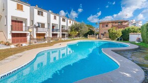 A swimming pool with a curved edge, surrounded by a paved area and a building with balconies.