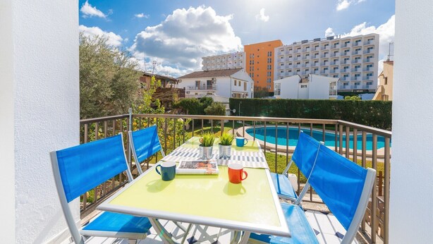 A balcony with a table, chairs, and a pool in the background.