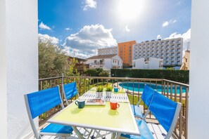 A balcony with a table, chairs, and a pool in the background. - Es Mallorqui - Apartment In Port D'alcúdia (Port D'alcúdia, Illes Balears)