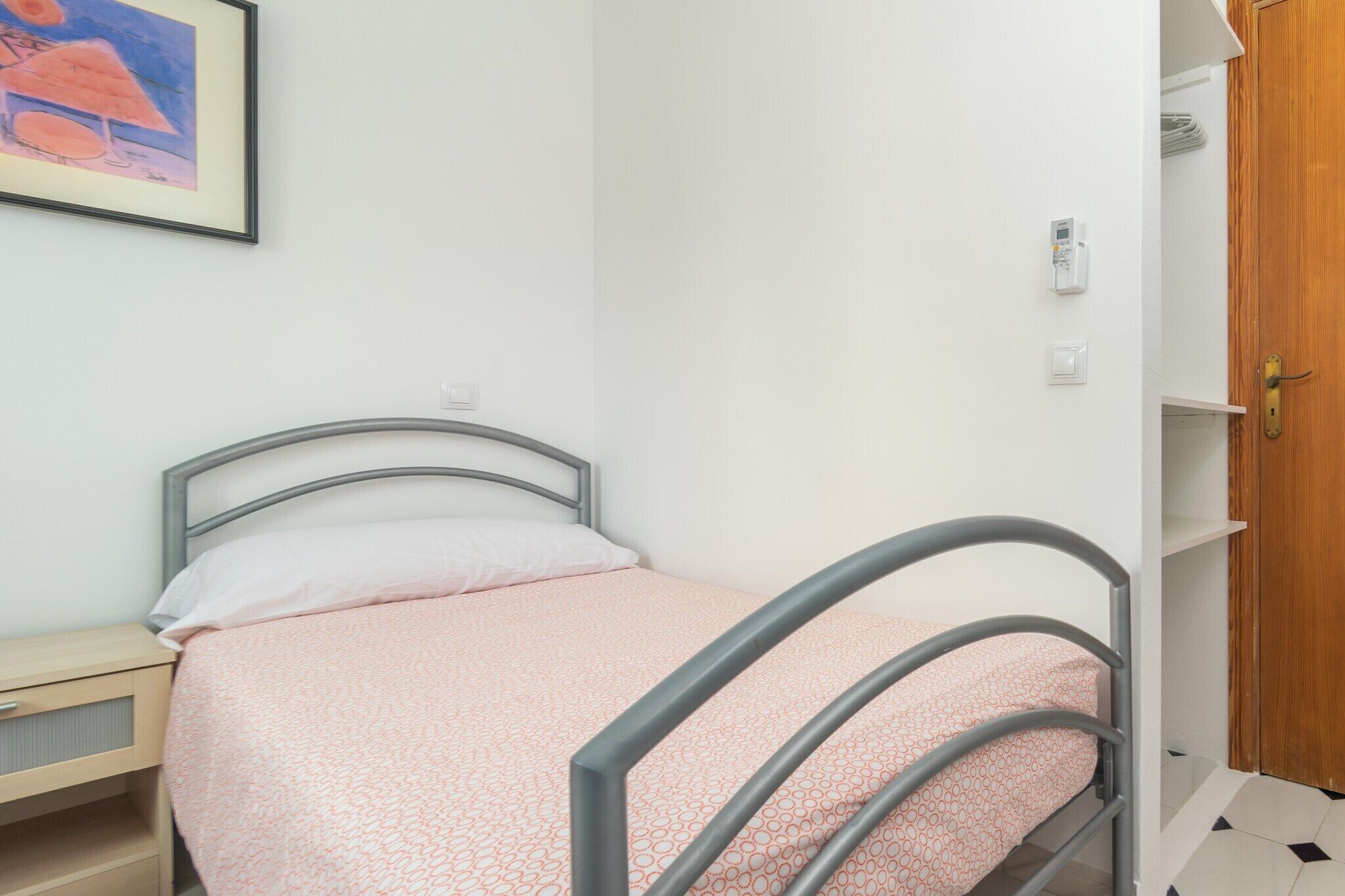 A single bed with a metal frame and a pink patterned bedspread in a small room with white walls.